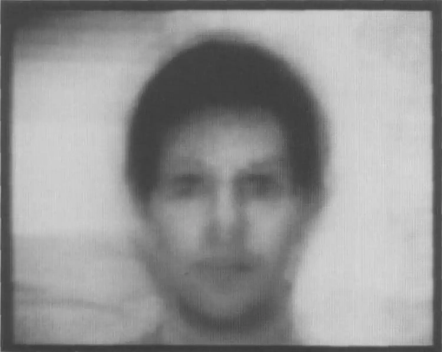 A greyscale image of that depicts a hazy male face with short, dark hair. 